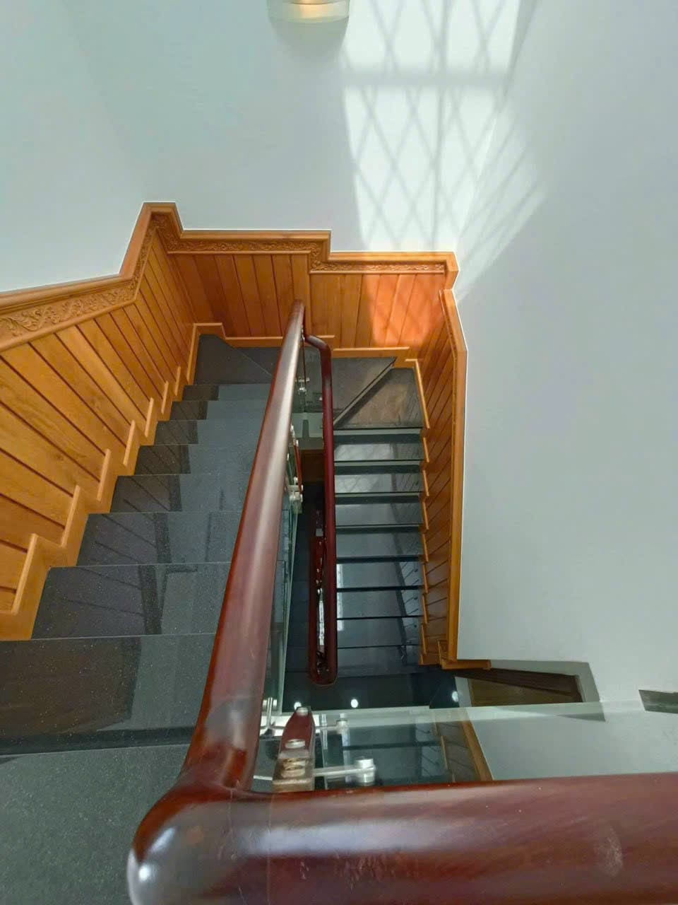 Cầu thang: ốp gỗ tường cầu thang có phào chỉ gỗ chạm hoa văn, mặt bậc đá granite đen, lan can kính cường lực tay vịn gỗ